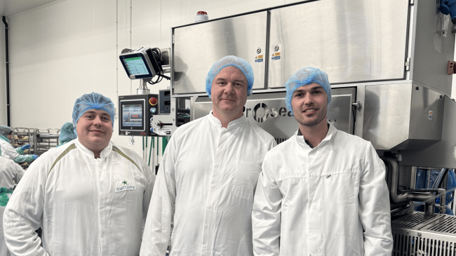 Three food industry professionals beside an industrial food processing machine at a production facility.