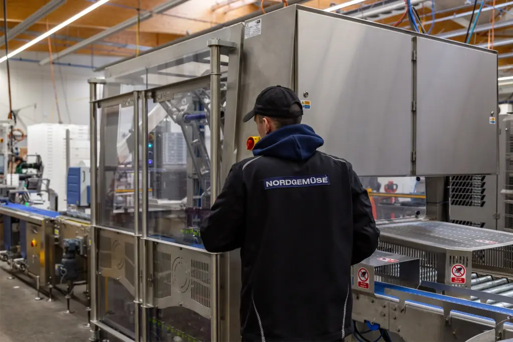 Nordgemüse employee operating an automated food packaging line in a vegetable processing facility.