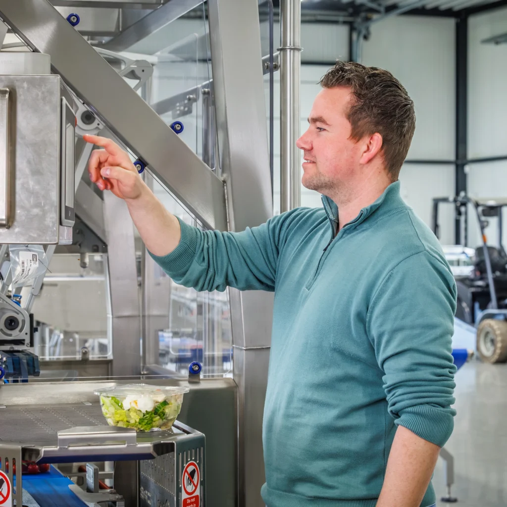 Sismatec specialist operating a touchscreen control panel on an automated industrial food packaging machine.